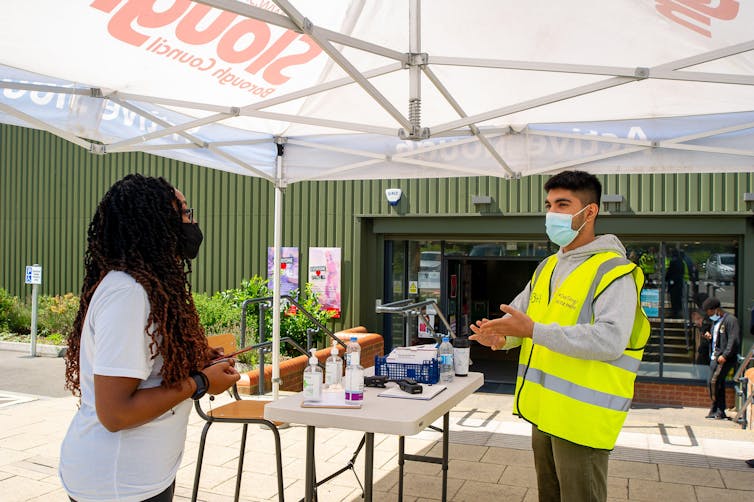 A young man and a young woman wearing masks in front of a registration table at a vaccine centre.