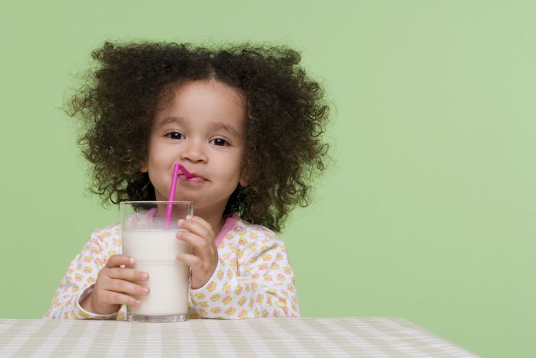 Una niña sonriente bebe de un vaso de leche con un popote.