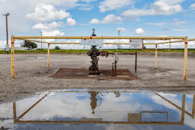 Wellhead surrounded by railings, with a large puddle nearby