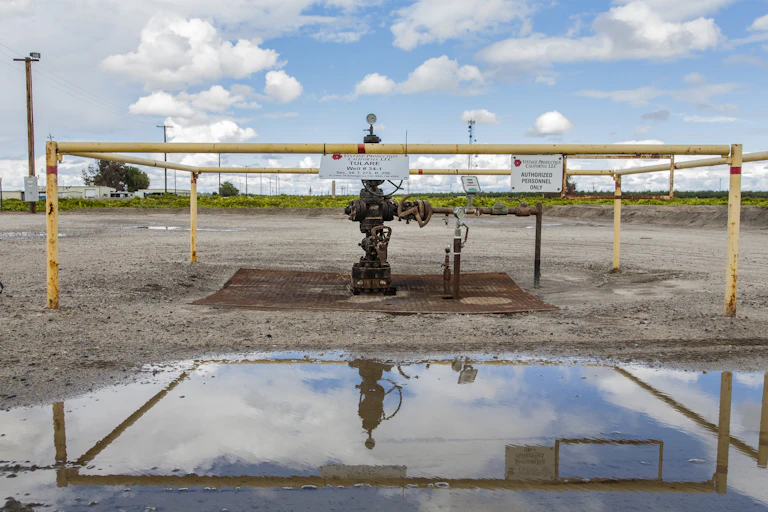 Wellhead surrounded by railings, with a large puddle nearby