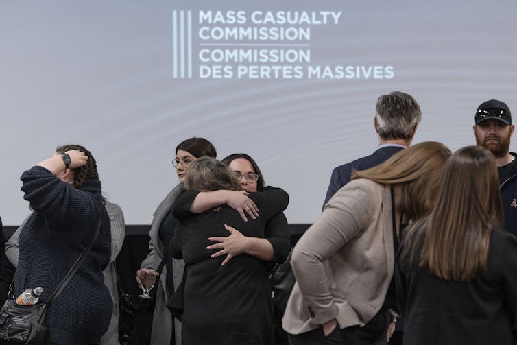 A group of people standing and embracing under a sign that reads: mass casualty commission in English and French