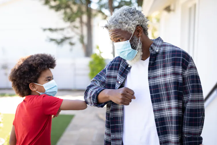 A man and his grandson wearing face masks touching elbows greeting social