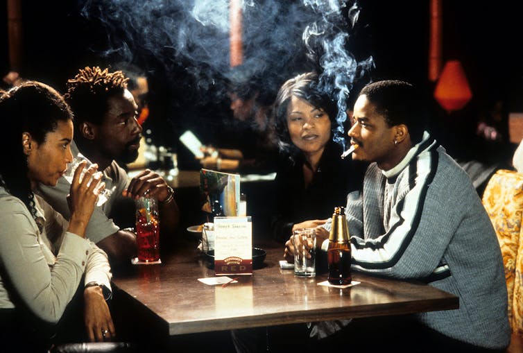Movie still of group of young adults smoking and drinking at a table