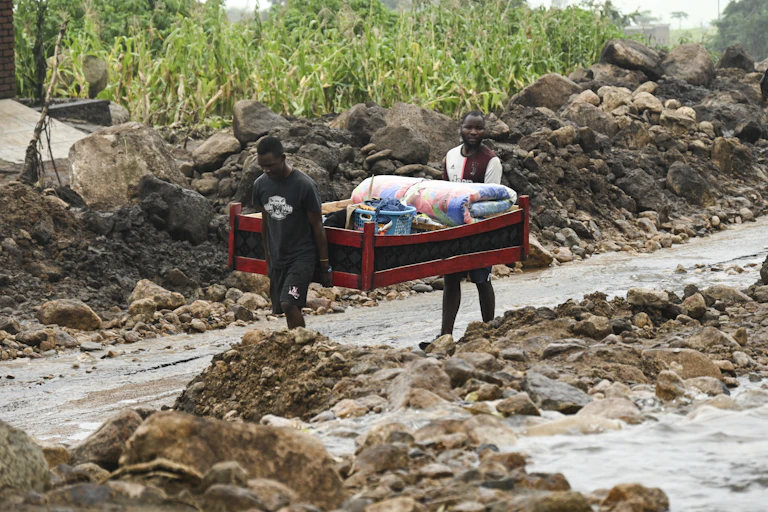 two men carry bed filled with belongings