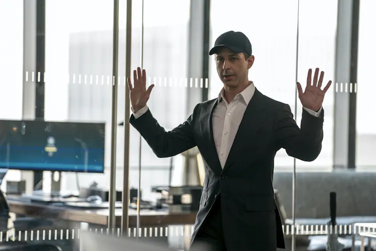 Kendall in a suit jacket, white shirt and baseball hat.