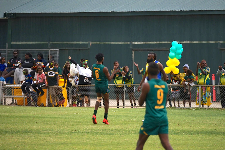 First Nations footballers on the field. They celebrate with the spectators who cheer.