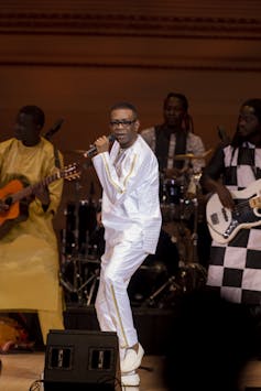 Un homme tout de blanc vêtu tenant un micro.