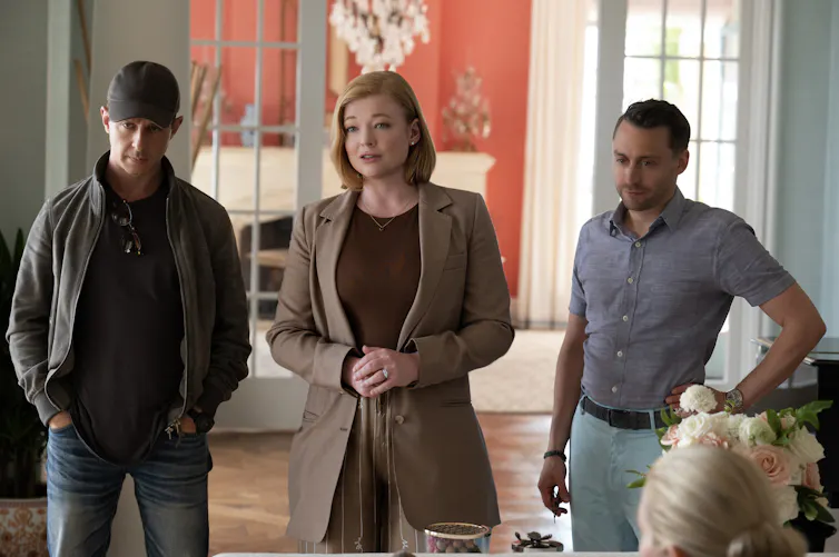 Two men and a woman standing in a beautiful airy room of a big house.