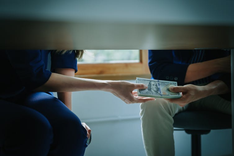 A person hands another person a stack of cash under a table.