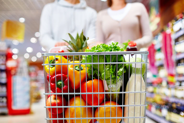 Image of cart full of products in supermarket being pushed by two people, shoulders down.