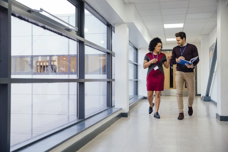 A man and a woman wearing lanyards discussing something while walking in a corridor