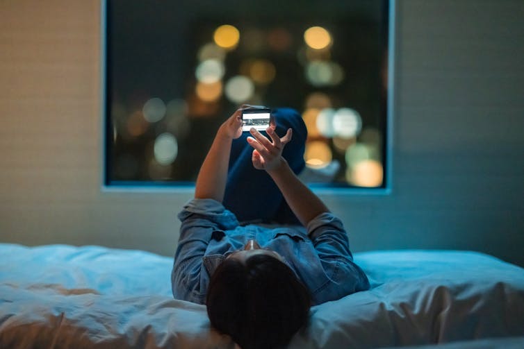 Woman lying on a bed and using a smart phone at night.
