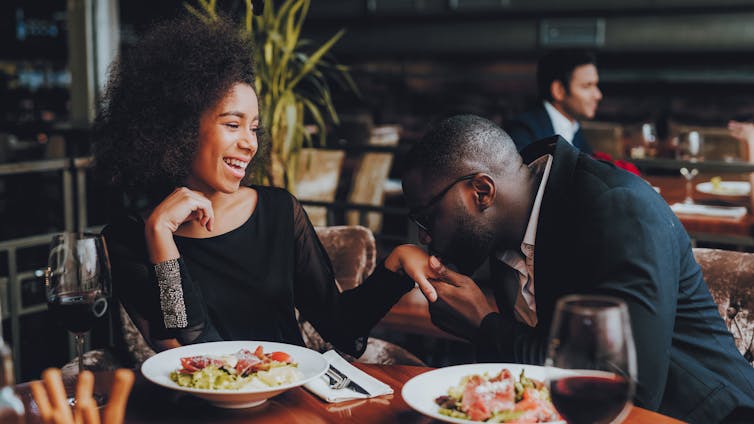 A man raises a woman's hand to his lips as they sit next to each other during a meal