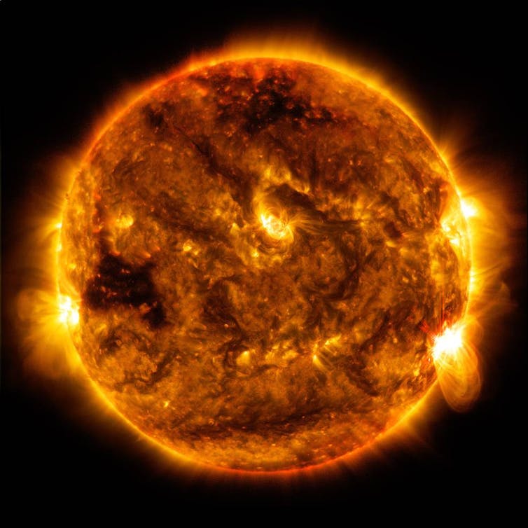 A image of the Sun as an orange ball with dark spots and bright loops.
