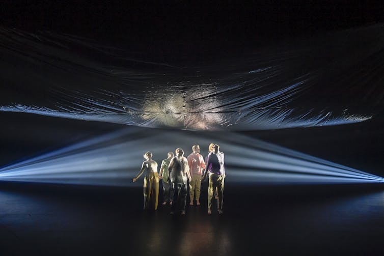 Six bodies look up at a blue sheet above their heads.