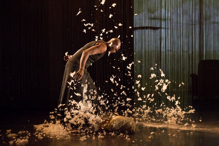 A Black woman dances surrounded by feathers.