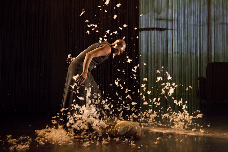 A Black woman dances surrounded by feathers.