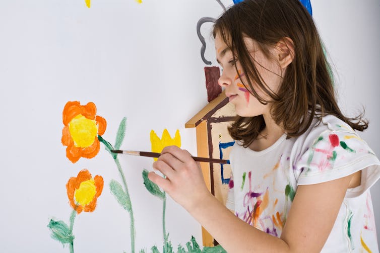 A child paints a flower on a wall.