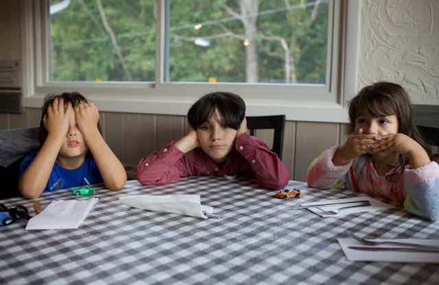 Three kids sitting at a table, each covering their eyes, ears and mouth.