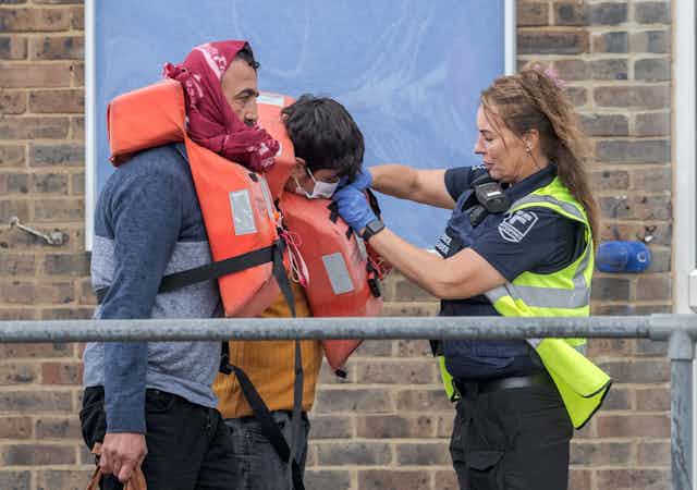 A female Border Force officer removes the life jackets of two male migrants who have arrived at Dover