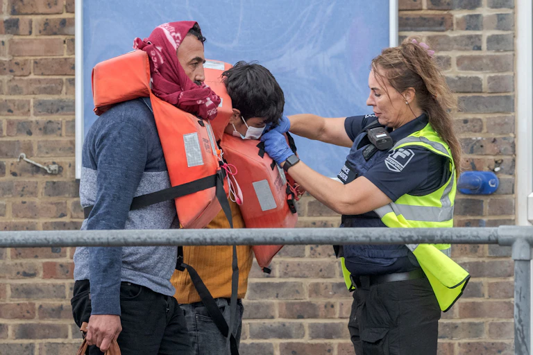 A female Border Force officer removes the life jackets of two male migrants who have arrived at Dover