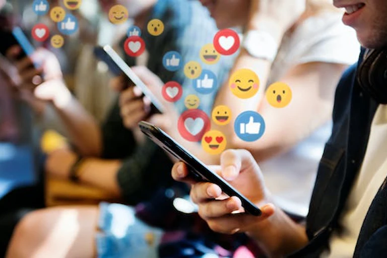 Des jeunes filles sourient en regardant leur téléphone portable, avec des "pouces en l'air", des "smileys" et des émojis "amour" qui sortent des écrans.