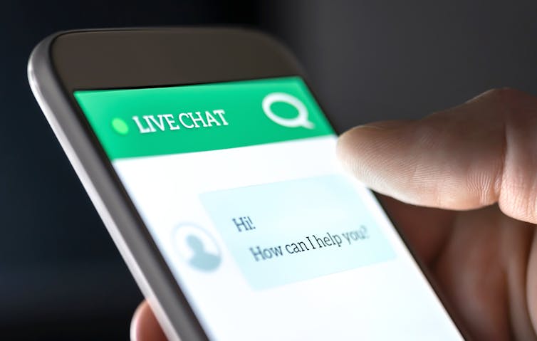 a hand holding a phonescreen showing a livechat with the text HI HOW CAN I HELP YOU?