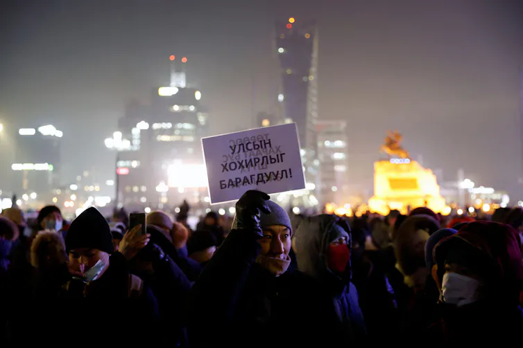 Protesters hold up banners against the skyline of Sukhbaatar Square in Ulaanbaatar, Mongolia December 2022.