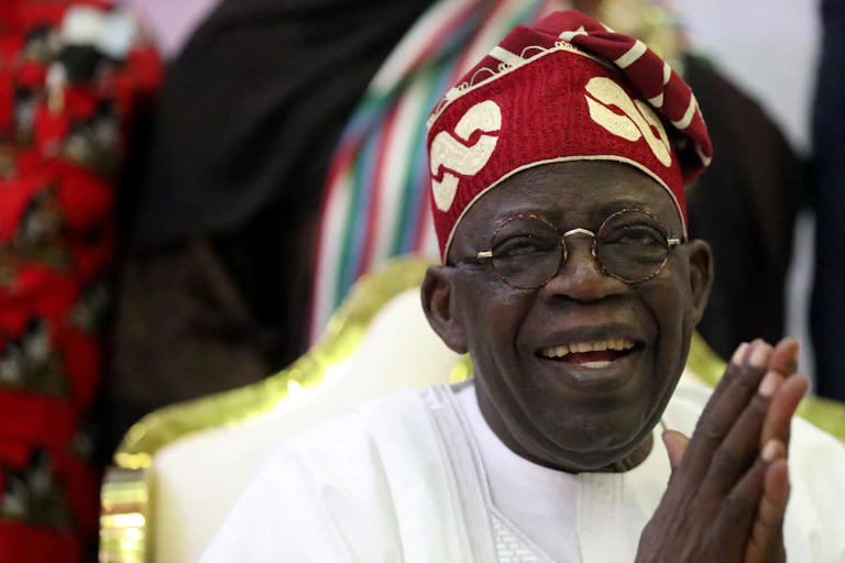 A man wearing a white robe and red cap smiling while holding his hands together.