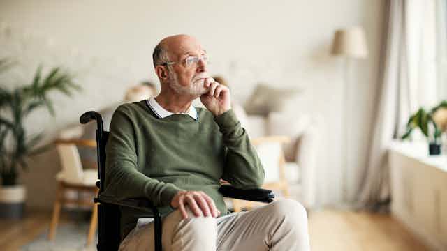 A senior man sitting in a wheelchair, appears pensive.