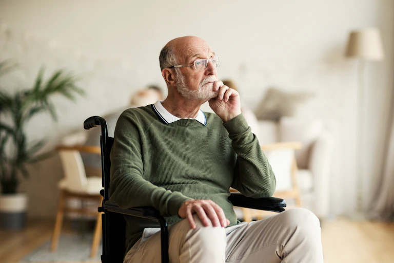 A senior man sitting in a wheelchair, appears pensive.