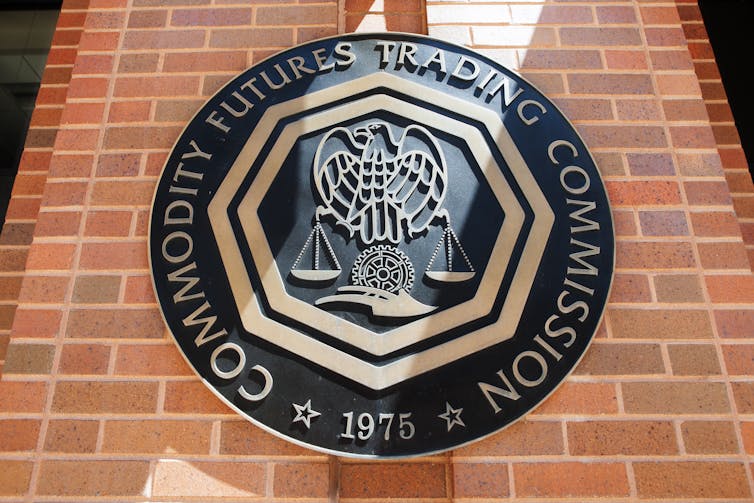 Black and gold emblem of the US Commodity Futures Trading Commission in Washington, DC, brick wall background.
