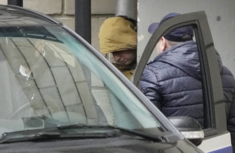 A man in a yellow hood is escorted into a car.