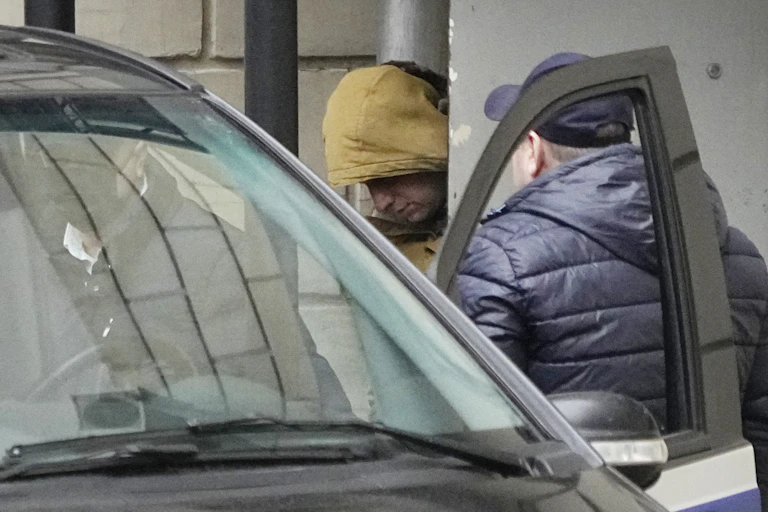 A man in a yellow hood is escorted into a car.