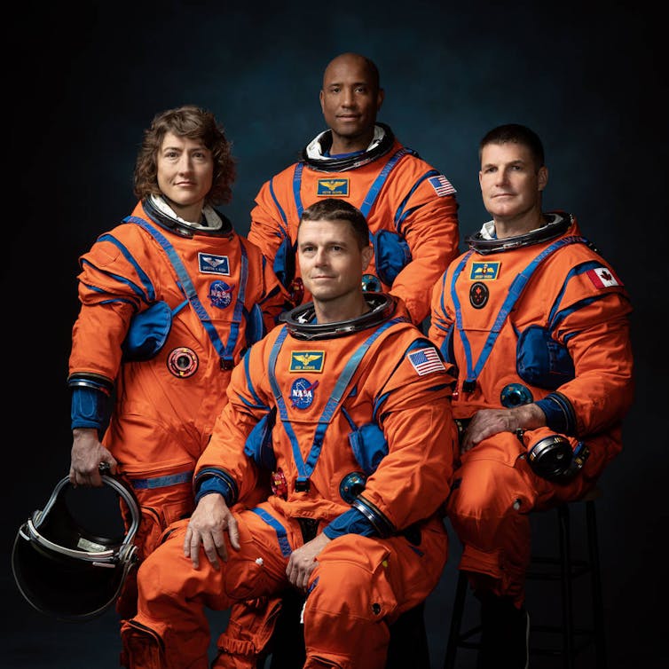 Czterech astronautów w pomarańczowych skafandrach kosmicznych i hełmach.