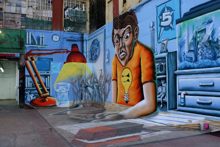 An oversized mural painted on the side of a building and on the ground of a person at a desk.