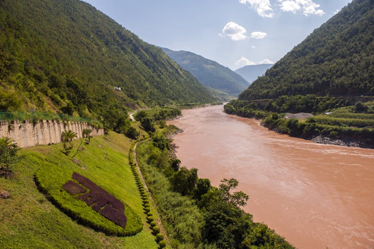 A brown river winds through a steep cliffs with a road and some buildings along the banks.