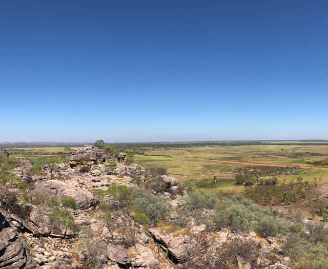 A panoramic photo of rocky land and a vegetation-covered floodplain beneath a blue sky.