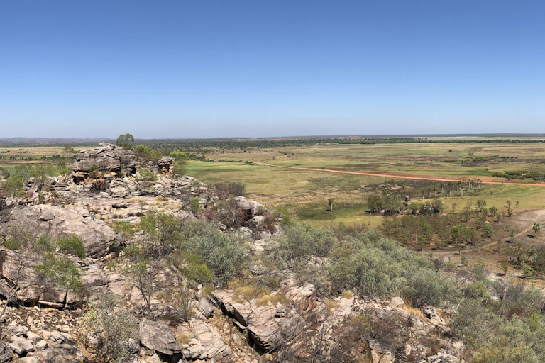 A panoramic photo of rocky land and a vegetation-covered floodplain beneath a blue sky.
