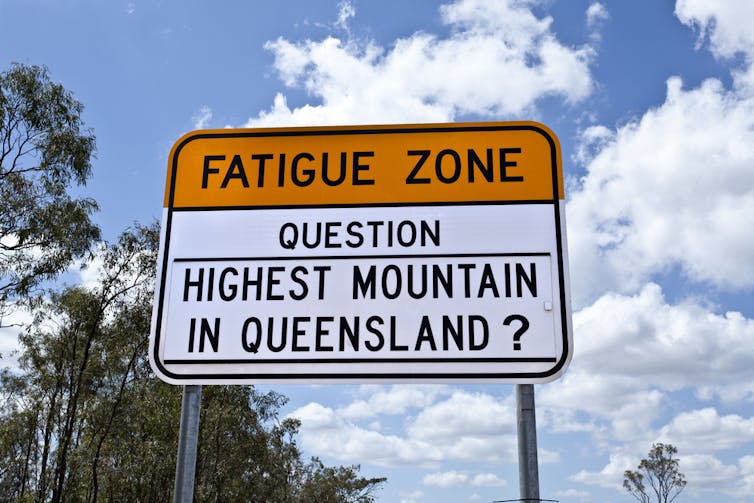 A road sign that reads 'fatigue zone question - highest mountain in Queensland?'