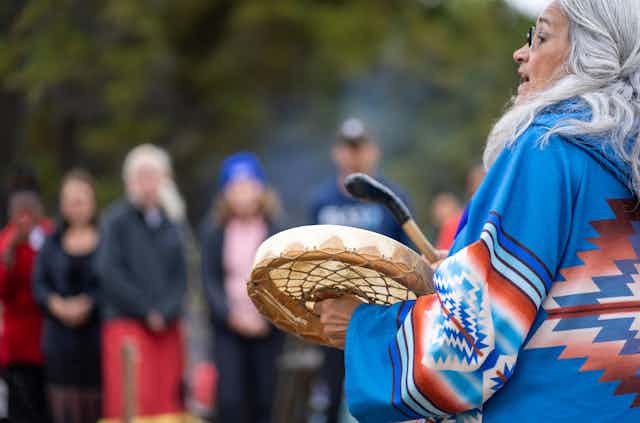 Women drumming by sacred fire attended by researchers