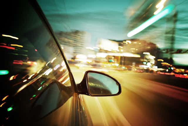 A car mirror at nighttime with blurry lights in the distance