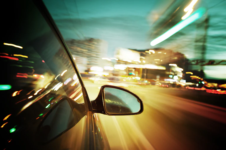 A car mirror at nighttime with blurry lights in the distance
