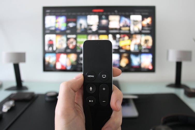 A hand holding a remote in front of a TV