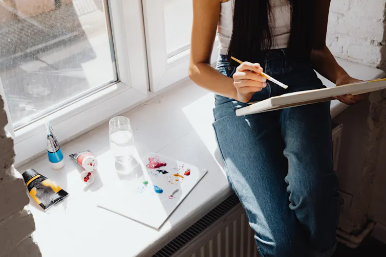 A young person sitting near a window, painting a canvas.