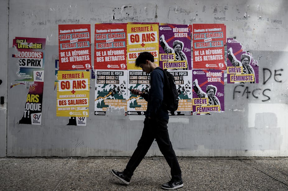 un étudiant marchant dans les couloirs d'une université où les murs sont couverts d'affiches appelant à la grève
