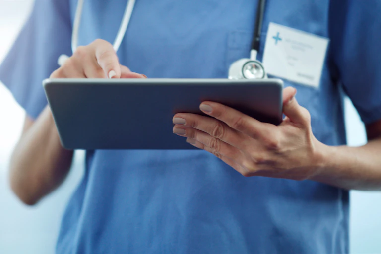 Close-up of health care provider in blue scrubs using tablet
