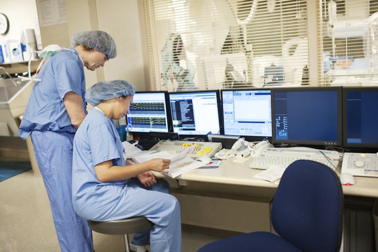 Two surgeons reviewing medical records in front of computer screens