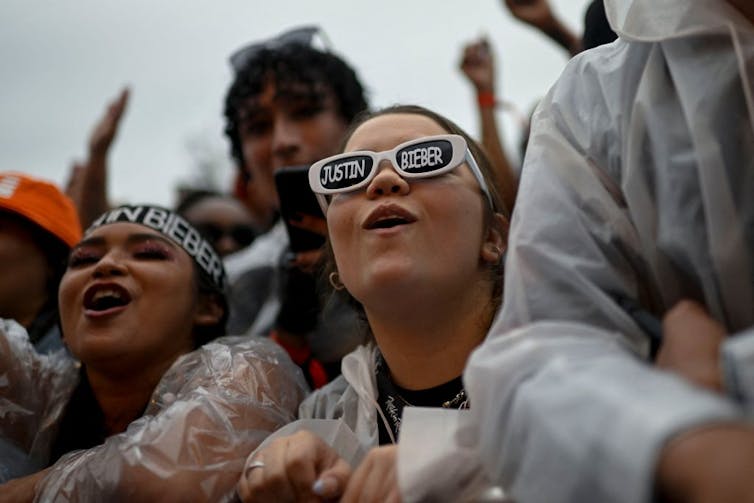 Woman at a concert wearing sunglasses that read 'Justin Bieber.'