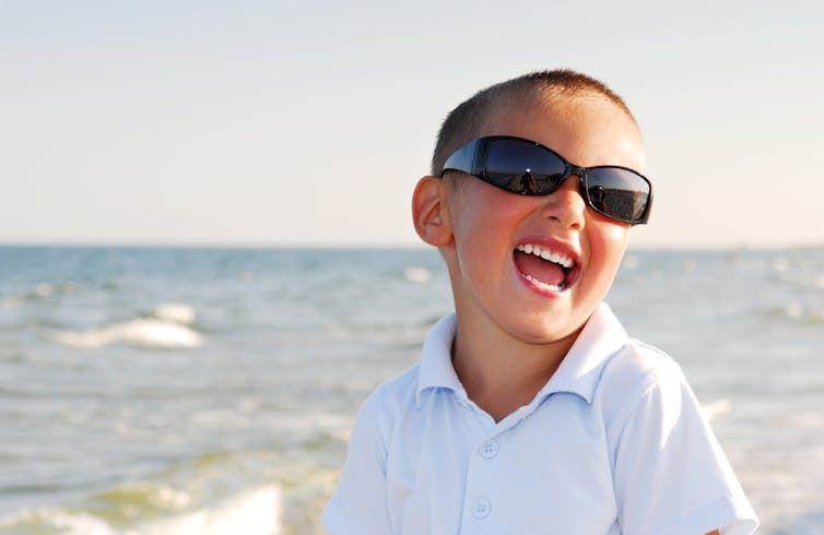 A child wears sunglasses on the beach.